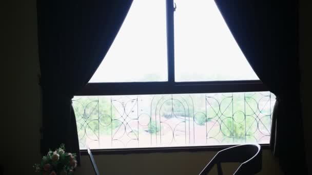 Silhouetten. Stuhl und Tisch mit Laptop und Blumen vor einem großen Fenster. außerhalb des Blicks auf das grüne Laub der Bäume — Stockvideo
