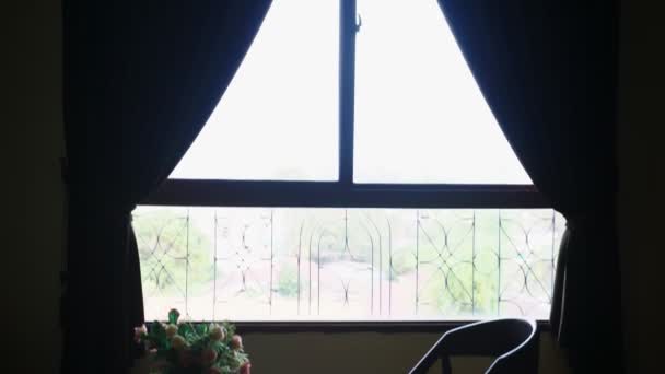 Silhuetas. cadeira e mesa com flores no fundo de uma grande janela. fora da vista da folhagem verde das árvores — Vídeo de Stock