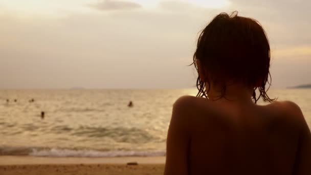 Силуэты, мальчик-подросток с вьющимися волосами смотрит в море на фоне морского пейзажа, красный драматический закат, в море солнце окрашивает море в красный цвет . — стоковое видео