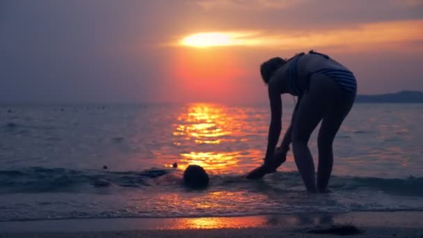 Olycka-konceptet. silhuetter, en kvinna drar en drunknad man från havet, mot bakgrund av havet landskap, en röd dramatiska solnedgången över havet. solen målar havet röd. — Stockvideo