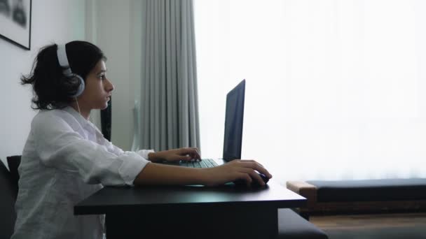 Adolescente juega videojuegos. Ordenador adolescente chico con auriculares mirando a la pantalla del ordenador portátil — Vídeo de stock