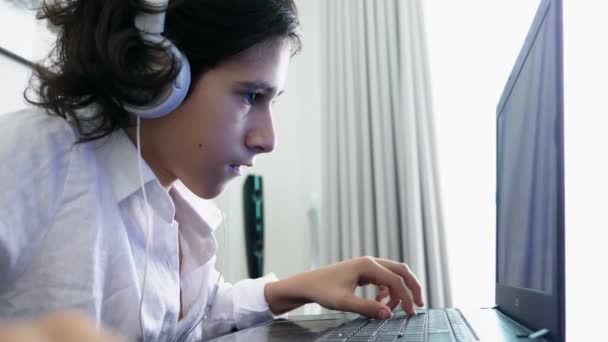 Adolescente juega videojuegos. Ordenador adolescente chico con auriculares mirando a la pantalla del ordenador portátil — Vídeo de stock