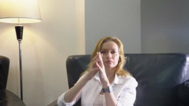 yakın çekim. Zarif bir kadın beyaz elbiseli bir büyük siyah deri sandalyede oturur, kameraya doğru görünüyor ve elleri bir jest, üstünlük, parmakları katlanmış bir kulenin ile gösterir. kopya alanı