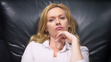 yakın çekim. Beyaz elbiseli, zarif bir kadın büyük siyah deri sandalyede oturan bir şey hakkında düşünüyor içine belgili tanımlık fotoğraf makinesi ve gülümsüyor görünüyor. kopya alanı