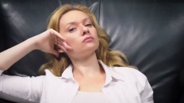 yakın çekim. Zarif bir kadın beyaz elbiseli bir büyük siyah deri sandalyede oturur. Bıkkın ve yorgun kadındır. kopya alanı