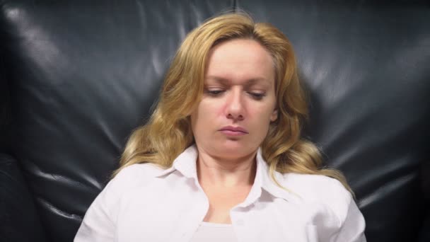 Nahaufnahme. Elegante Frau im weißen Anzug sitzt in einem großen schwarzen Lederstuhl und niest. Kopierraum — Stockvideo