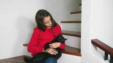 Gülümseyen ve bir kedi yavrusu kucağında tutan güzel genç kız kırmızı kazak ve terry çorap ve kot, merdivenlerde, oturma