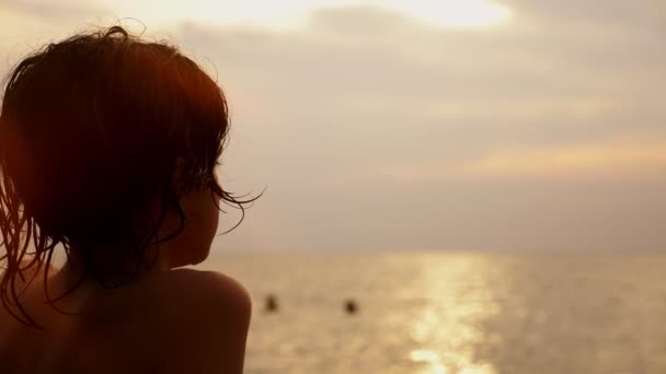 Siluetas, adolescente con pelo rizado mira en el mar contra el telón de fondo del paisaje marino, rojo dramático atardecer, en el mar el sol pinta el mar en rojo . — Vídeo de stock