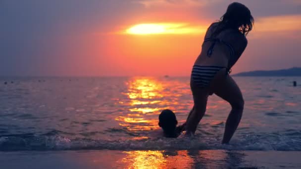 Concepto de accidente. siluetas, una mujer tira de un hombre ahogado del mar, contra el telón de fondo del paisaje marino, una puesta de sol dramática roja sobre el mar. el sol pinta el mar de rojo . — Vídeos de Stock