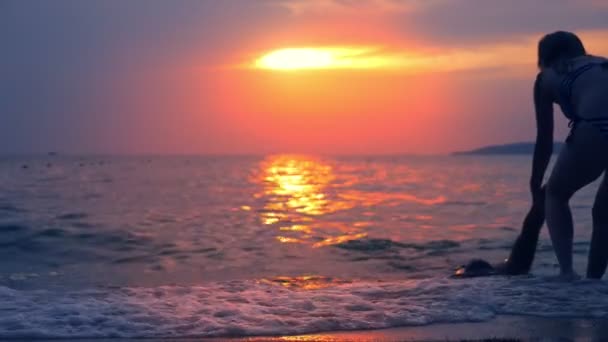 Έννοιας ατύχημα. σιλουέτες, τραβάει μια γυναίκα τοπίο ενός Πνιγμένου από τη θάλασσα, με φόντο τη θάλασσα, ένα κόκκινο εντυπωσιακό ηλιοβασίλεμα πάνω από τη θάλασσα. ο ήλιος βάφει κόκκινο στη θάλασσα. — Αρχείο Βίντεο