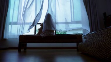 little teenager looking out of the window in bad weather, silhouette of a fragile teenager girl on the background of a large window clipart