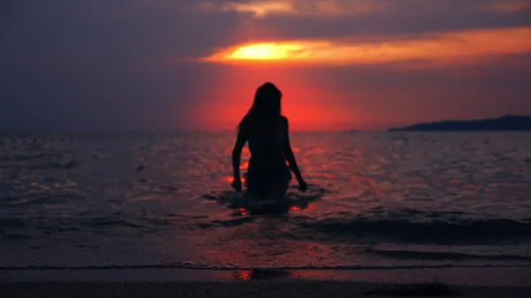 Silueta de una mujer que emerge del mar contra el telón de fondo del paisaje marino, una puesta de sol dramática roja en el mar el sol pinta el mar rojo . —  Fotos de Stock