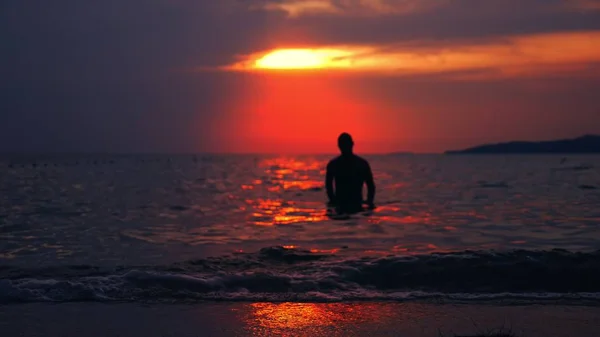 Silueta de un hombre en forma que emerge del mar contra el telón de fondo del paisaje marino, una puesta de sol dramática roja en el mar el sol pinta el mar rojo . —  Fotos de Stock