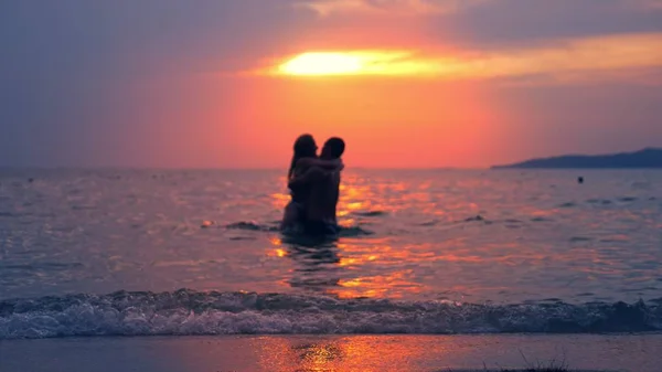 Siluetas, pareja, hombre y mujer fuera del mar tomados de la mano contra el fondo del paisaje marino, rojo dramático atardecer en el mar. el sol tiñe el mar de rojo . —  Fotos de Stock