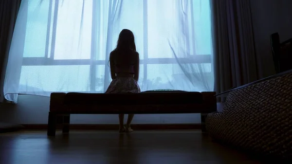 Kleiner Teenager, der bei schlechtem Wetter aus dem Fenster schaut, Silhouette eines fragilen Teenagermädchens auf dem Hintergrund eines großen Fensters — Stockfoto