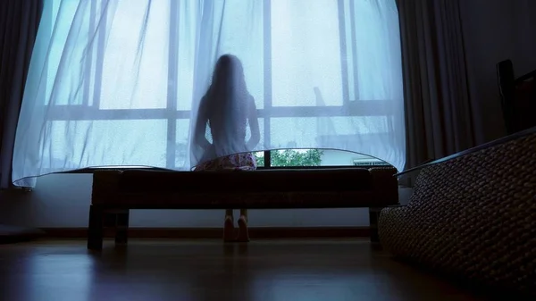 Little teenager looking out of the window in bad weather, silhouette of a fragile teenager girl on the background of a large window — Stock Photo, Image