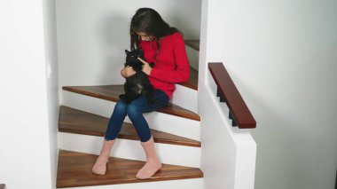 Gülümseyen ve bir kedi yavrusu kucağında tutan güzel genç kız kırmızı kazak ve terry çorap ve kot, merdivenlerde, oturma