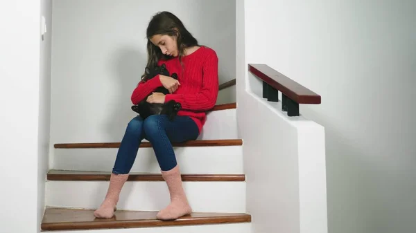 Menina adolescente bonita em camisola vermelha e meias terry e jeans, sentado nas escadas, sorrindo e segurando um gatinho em seu colo — Fotografia de Stock