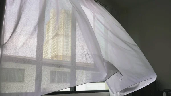 Transparent window curtain, gently moved by the wind. outside the window you can see the skyscrapers