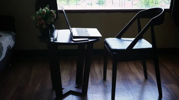 Силуэты. стул и стол с ноутбуком и цветами на фоне большого окна. за пределами вида зеленой листвы деревьев — стоковое фото