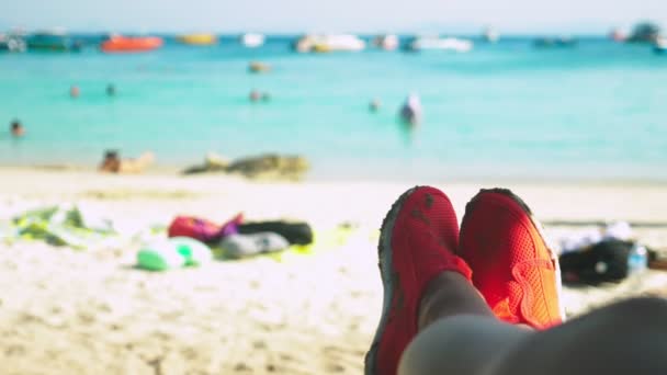 Close-up van vrouwelijke benen in rode schoenen om te zwemmen op de achtergrond van het azuurblauwe strand, achtergrond wazig — Stockvideo