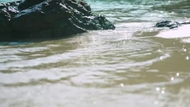 Κινηματογράφηση σε πρώτο πλάνο από πέτρες σε μια αμμώδη παραλία που βρέχεται από ένα κύμα της θάλασσας — Αρχείο Βίντεο