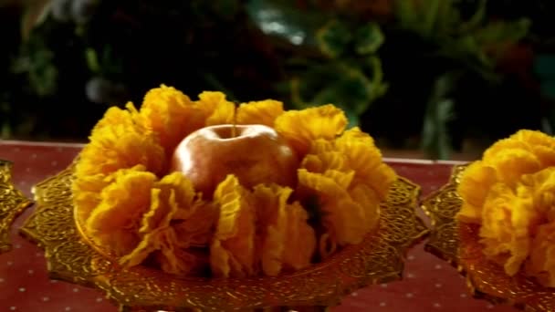 Nahaufnahme, traditionelle buddhistische Opfergaben. Apfel im goldenen Ständer mit gelben Blüten — Stockvideo