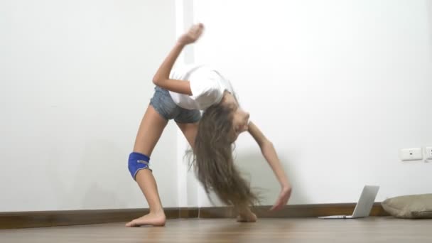 Flexibilidad y fuerza. hermosa chica joven con el cuerpo perfecto estiramiento de los músculos en casa, mientras que mirando la lección de estiramiento en línea en un ordenador portátil — Vídeo de stock