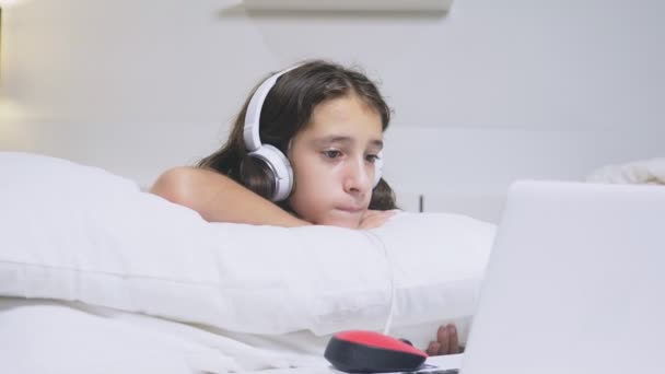 Дівчина-підліток в навушниках шокує те, що відбувається на екрані її ноутбука, тому що вона була сама. концепція безпеки інтернету для дітей — стокове відео