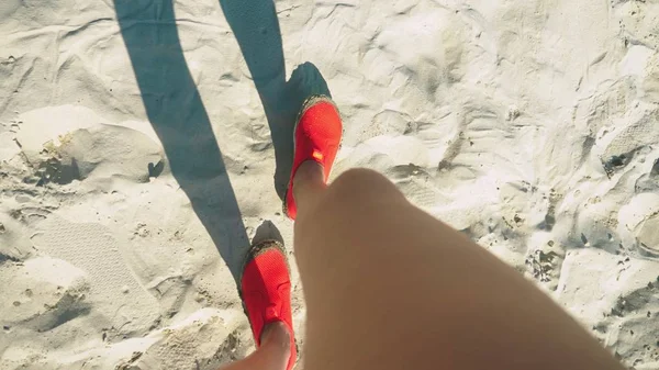 Close-up de pernas femininas em sapatos vermelhos para nadar andando em uma praia de areia branca — Fotografia de Stock