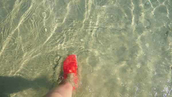 Close-up de pernas femininas em sapatos vermelhos para nadar andando em uma praia de areia branca — Fotografia de Stock