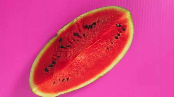 As mãos femininas apanham uma melancia com um fundo rosa brilhante. Conceito mínimo de fruta . — Fotografia de Stock