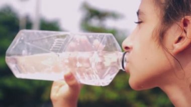 yakın çekim. bir kız yeşil yaprakların bir arka plan üzerinde plastik bir şişe temiz su içiyor