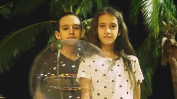 Chica feliz y adolescente niño sosteniendo un gran globo aireado, brillante en las manos, sobre el fondo de las palmeras. Hora de la tarde. concepto de turismo y vacaciones en la playa . — Vídeo de stock