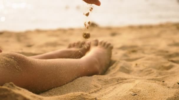 腿上的女孩在海滩上倒沙子在她的脚 — 图库视频影像