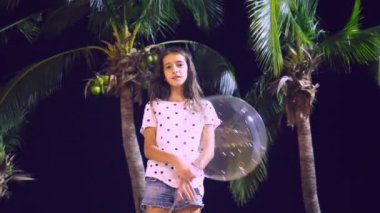 mutlu genç kız büyük havadar, parlayan balon palmiye ağaçları arka planı onun elinde tutan. akşam saat. Turizm ve plaj tatil kavramı.