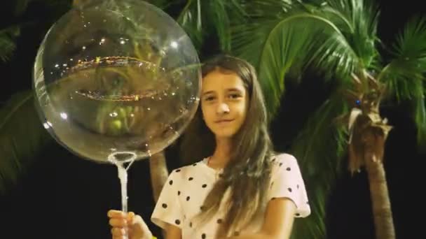 Gelukkig tiener meisje bedrijf grote luchtige, gloeiende ballon in haar handen tegen de achtergrond van palmbomen. 's avonds de tijd. concept van toerisme en strand vakantie. — Stockvideo