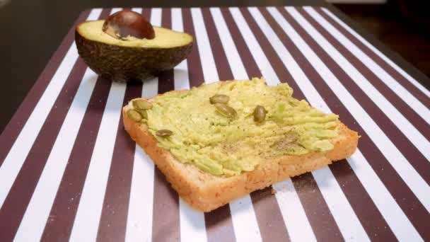 Aguacate sobre pan tostado con especias sobre un fondo blanco negro rayado. El concepto de alimentación saludable . — Vídeos de Stock