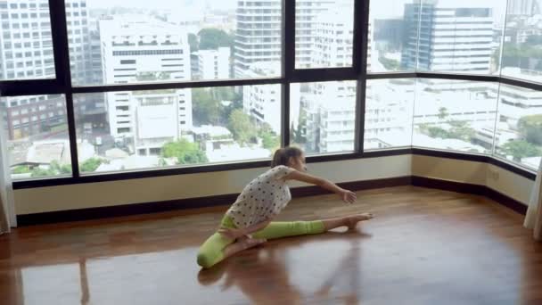 Delgada joven estirándose frente a una gran ventana panorámica con vistas a los rascacielos — Vídeos de Stock
