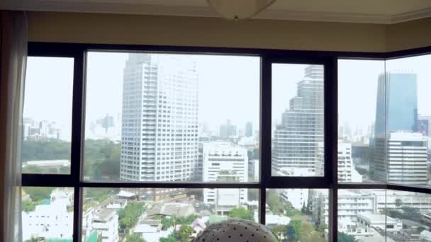 Delgada joven estirándose frente a una gran ventana panorámica con vistas a los rascacielos — Vídeos de Stock