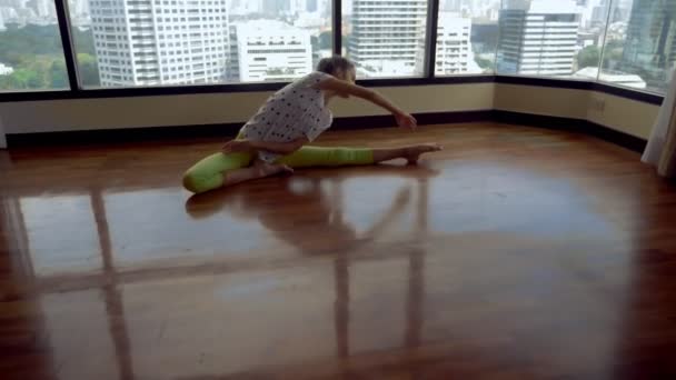 Slim young girl stretching in front of a large panoramic window overlooking the skyscrapers — Stock Video