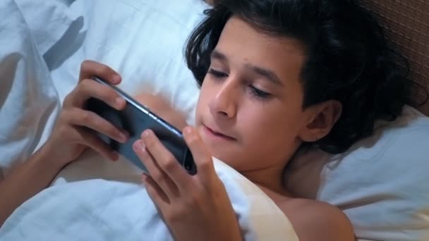 Tiener jongen maakt gebruik van smartphone op bed voordat slapen 's nachts. Mobiele verslaafde concept. — Stockvideo