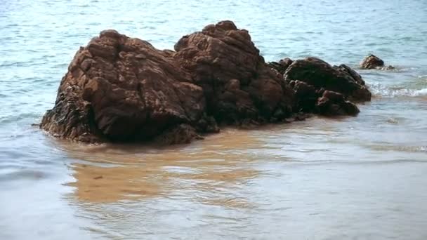 Камень на песчаном пляже, омываемый морскими волнами — стоковое видео