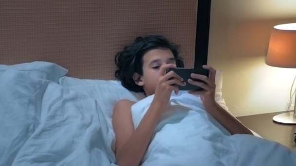 Teen boy uses smartphone on bed before sleep at night. Mobile addict concept. — Stock Video