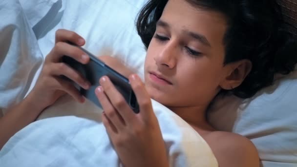 Teen boy uses smartphone on bed before sleep at night. Mobile addict concept. — Stock Video