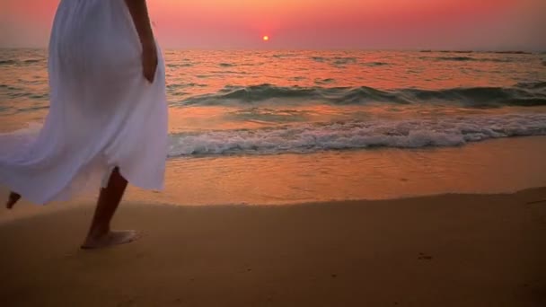 女孩在一个长的白色礼服与长头发在日落时沿着海滨散步 — 图库视频影像