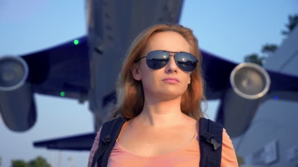 観光の概念 彼女の背中にバックパックでサングラスの女性観光客が飛行機の背景に空港へ行きます 空港で笑顔の女性金髪 — ストック動画
