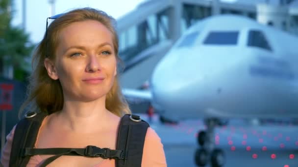 観光の概念。彼女の背中にバックパックでサングラスの女性観光客が飛行機の背景に空港へ行きます。空港で笑顔の女性金髪 — ストック動画