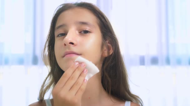 Conceito de cuidados da pele adolescente. adolescente menina limpa a pele do rosto com um cotonete com loção . — Vídeo de Stock