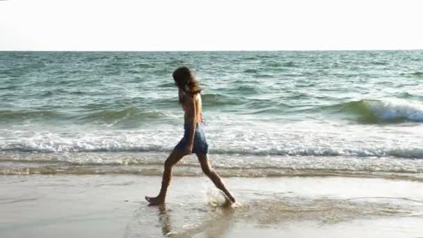 Χαριτωμένος έφηβος κορίτσι τρέχει μια χαρά κατά μήκος της παραλίας ξυπόλυτος — Αρχείο Βίντεο